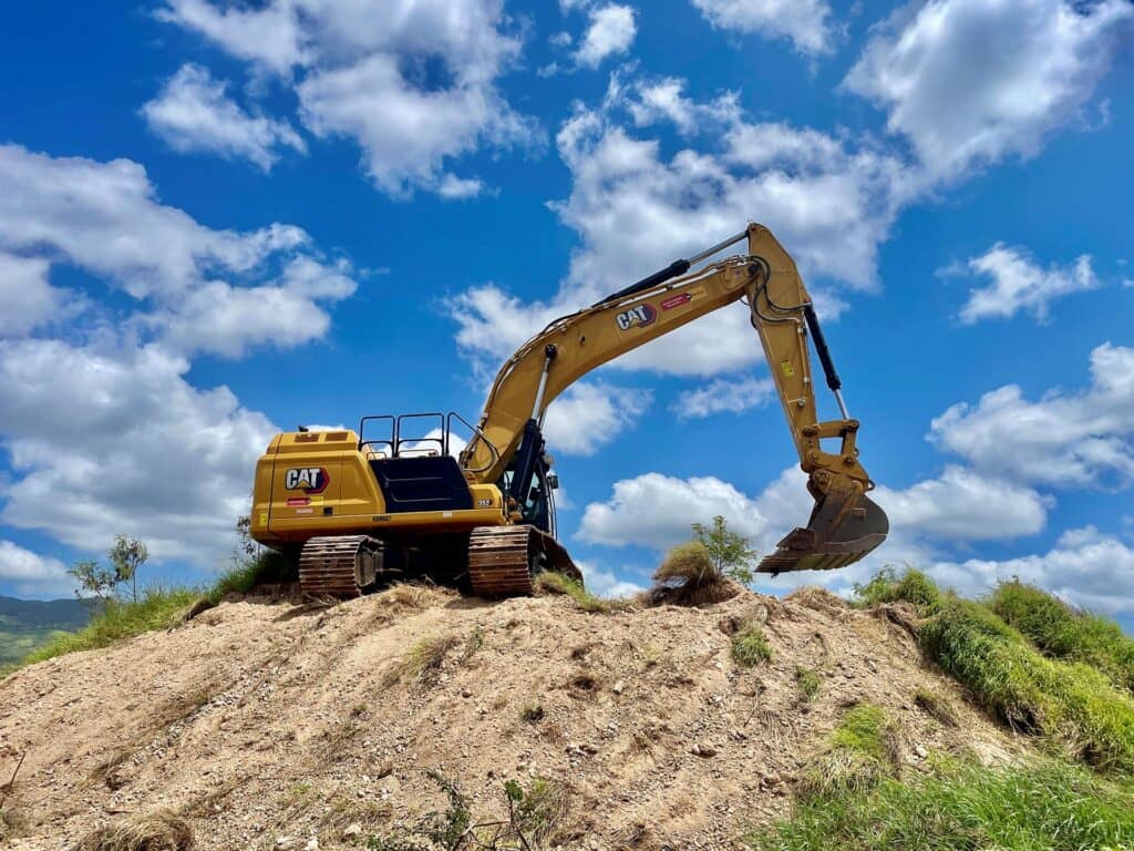 Excavator on a dirt mound under clouds